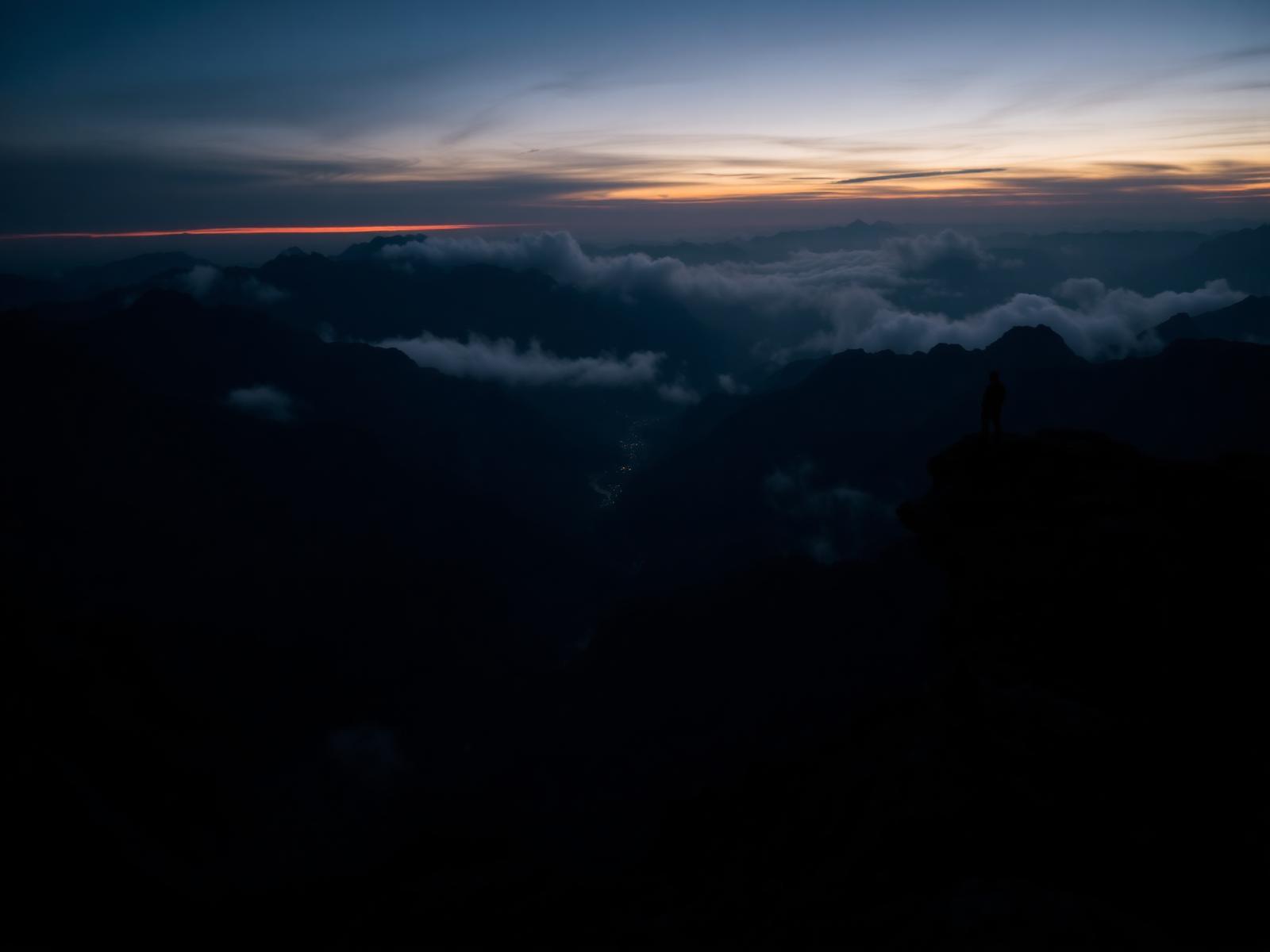 Silhouette on cliff overlooking mountains at dusk